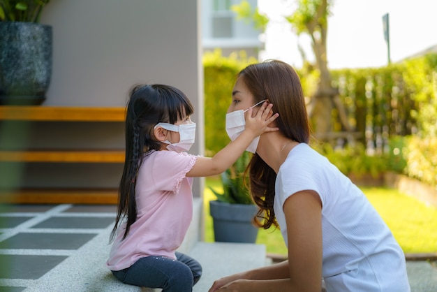 La madre asiatica aiuta sua figlia che indossa la maschera di protezione
