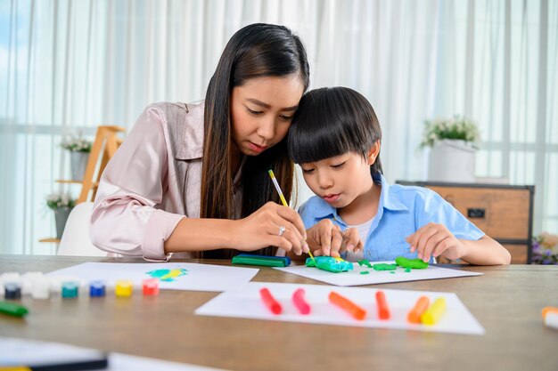 La madre asiatica lavora a casa insieme al figlio. Mamma e bambino giocano con la pasta. Bambino che crea un modello in plastilina. Stile di vita della donna e attività familiare.