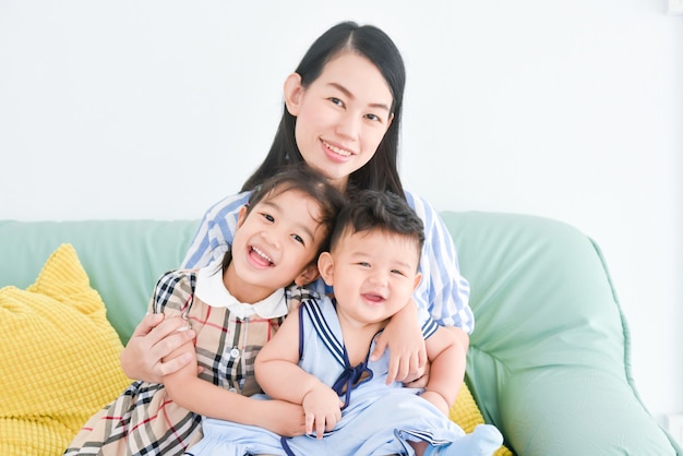 La madre asiatica sorride mentre tiene il suo bambino piccolo e abbraccia sua figlia. Madre felice con i bambini.