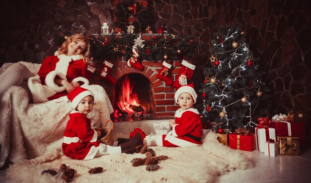 La madre con i bambini è seduta vicino al caminetto e gioca con i coni - decorazioni natalizie