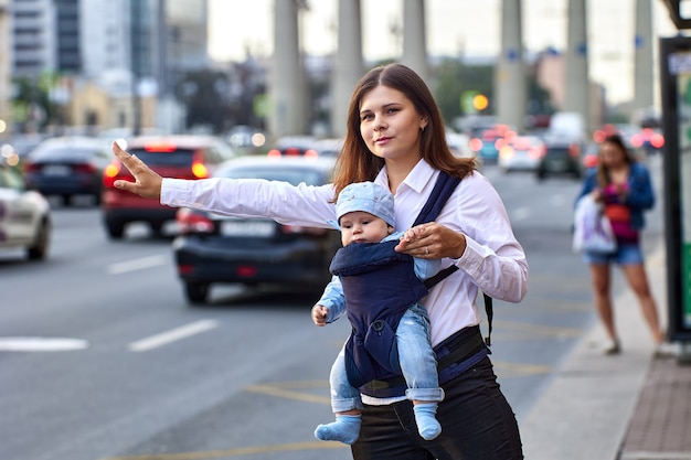 La madre con il bambino in fascia sta fermando un taxi vicino al traffico