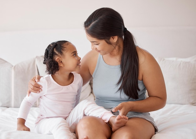 La madre con la bambina parla sul letto, sorride e ama insieme nella camera da letto di casa Donna felice o mamma e giovane bambino carino che sorridono e si divertono con il legame giocoso e la conversazione come famiglia al mattino a casa