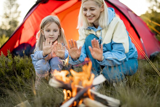 La madre con la figlia si siede vicino al fuoco vicino alla tenda sulla natura