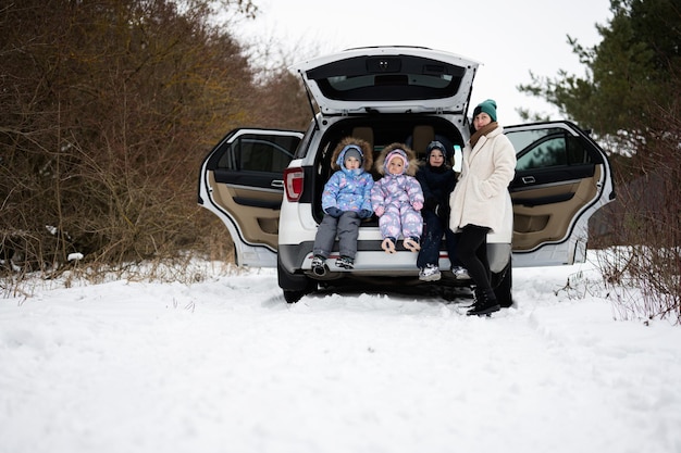 La madre con tre bambini si siede sul suv dell'automobile con il supporto del bagagliaio aperto nella foresta invernale