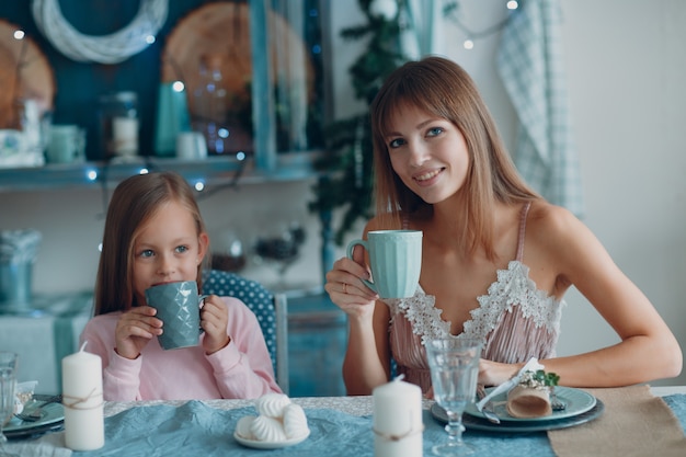 La madre con una figlia piccola si siede e fa colazione al tavolo in cucina. Stare a casa.