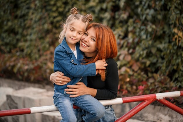 La madre dai capelli rossi alla moda e sua figlia stanno parlando calorosamente. Bambino felice e sua madre per strada. Madre single di successo con sua figlia a fare una passeggiata. Caloroso rapporto familiare