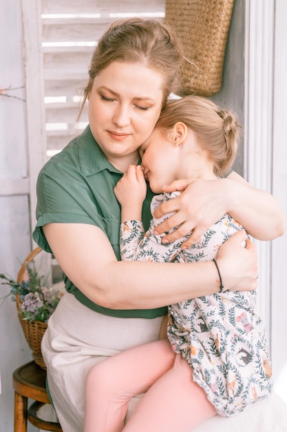 La madre di famiglia felice con la figlia del bambino si diverte nella vita domestica della campagna suburbana in una giornata di sole la mamma candida tiene il bambino tra le braccia e le ginocchia e gli abbracci e si sente dispiaciuto che le persone amano e si prendono cura del momento