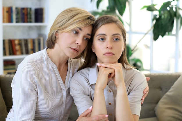 La madre di mezza età preoccupata e la figlia adulta si siedono sul divano conversando seriamente, ascoltano i suoi problemi di condivisione.