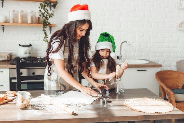 La madre e il bambino allegri felici in cappelli di Babbo Natale stanno cucinando i biscotti di Natale in cucina il nuovo anno e il Natale