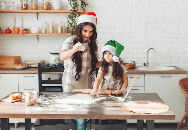 La madre e il bambino allegri felici in cappelli di Babbo Natale stanno cucinando i biscotti di Natale in cucina il nuovo anno e il Natale