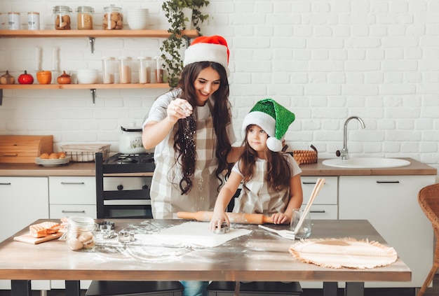La madre e il bambino allegri felici in cappelli di Babbo Natale stanno cucinando i biscotti di Natale in cucina il nuovo anno e il Natale