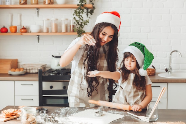 La madre e il bambino allegri felici in cappelli di Babbo Natale stanno cucinando i biscotti di Natale in cucina il nuovo anno e il Natale