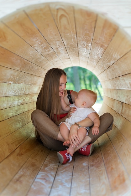 La madre e il bambino sono seduti all'interno del tunnel di legno sul parco giochi. Telaio verticale