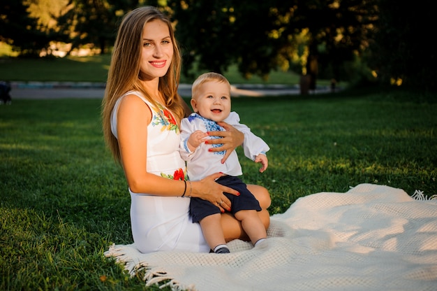 La madre e il suo bambino vestito con le tradizionali camicie ricamate seduto sul plaid nel parco