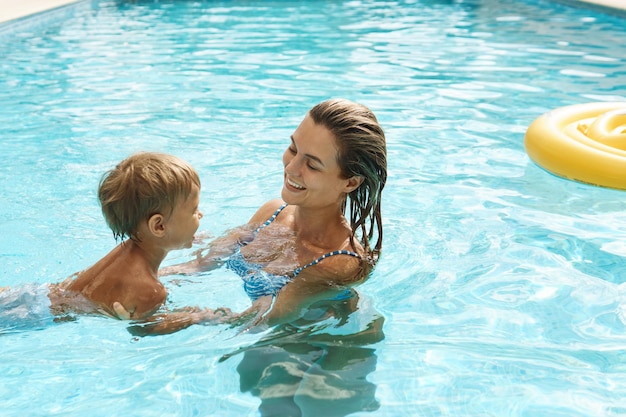 La madre e il suo piccolo figlio carino nuotano nella piscina all'aperto durante le vacanze estive