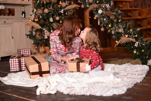 La madre e la figlia che si siedono sul pavimento vicino all'albero di Natale