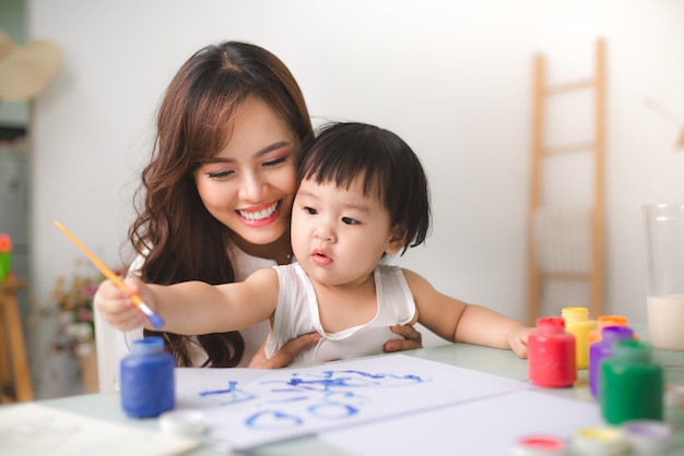 La madre e la figlia felici della famiglia dipingono insieme. La donna asiatica aiuta la sua bambina.