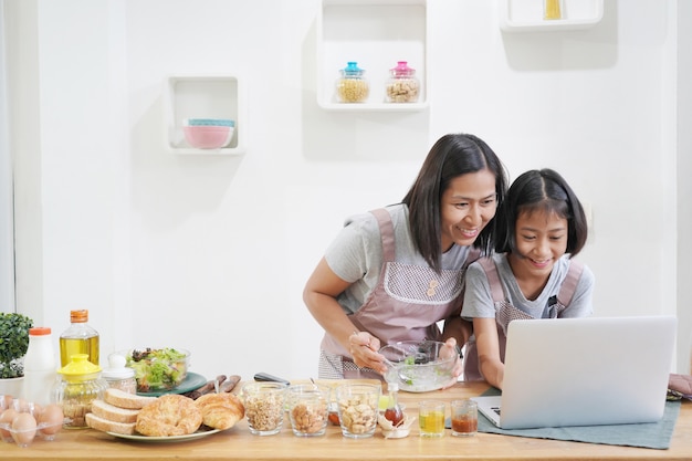 La madre e la figlia impara la cottura facendo uso del computer portatile nella cucina a casa