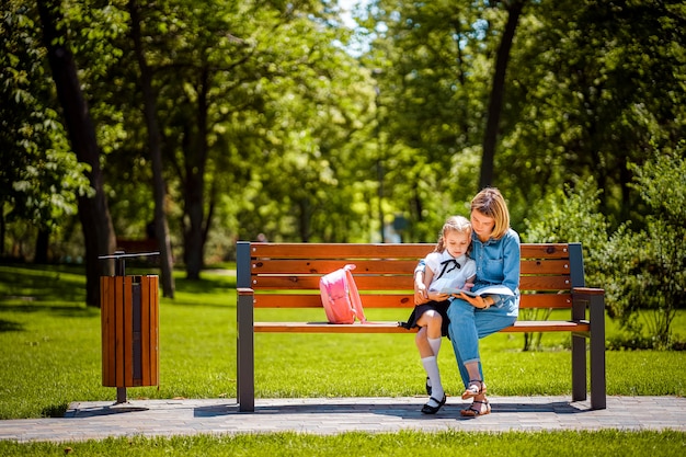 La madre e la piccola figlia in parco pubblico all'aperto che si siedono sul banco e leggono il libro