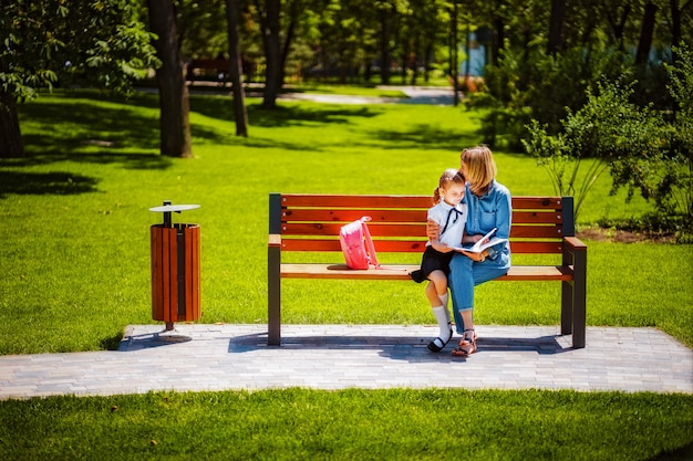 La madre e la piccola figlia in parco pubblico all'aperto che si siedono sul banco e leggono il libro