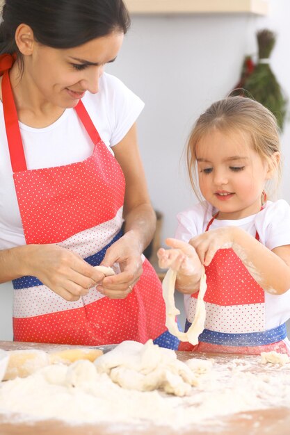 La madre e la sua graziosa figlia preparano l'impasto al tavolo di legno Pasticceria fatta in casa per pane o pizza Sfondo di panetteria