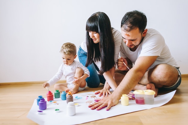 La madre felice del padre di arte della famiglia di gioia e le mani di manifestazione del figlio nei colori luminosi dipingono insieme l&#39;arte dell&#39;immagine