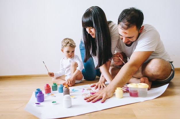 La madre felice del padre di arte della famiglia di gioia e le mani di manifestazione del figlio nei colori luminosi dipingono insieme l&#39;arte dell&#39;immagine