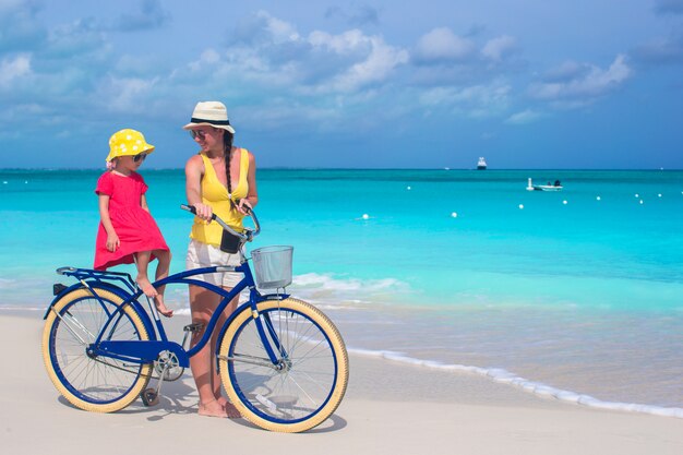 La madre felice e sua figlia che guidano vanno in bicicletta su una spiaggia tropicale