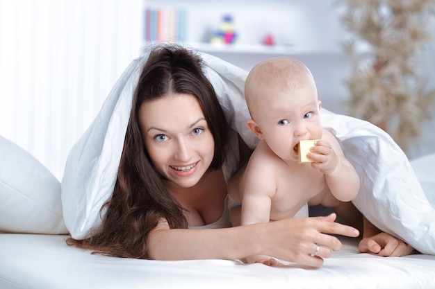 La madre felice gioca con il bambino sdraiato sul letto. il concetto di educazione