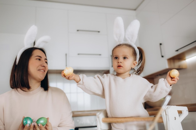 La madre felice insegna alla figlia del bambino a dipingere le uova di pasqua