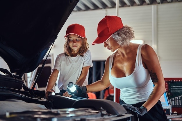 La madre insegna a sua figlia come riparare il motore dell'auto rotto in officina.