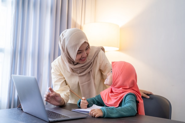 La madre musulmana asiatica aiuta sua figlia a imparare online usando il laptop studiando da casa