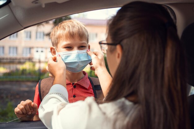 La madre premurosa aiuta il suo piccolo figlio a indossare una maschera protettiva medica