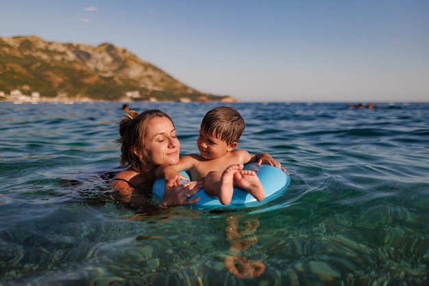 La madre premurosa cavalca suo figlio su un anello gonfiabile nel mare