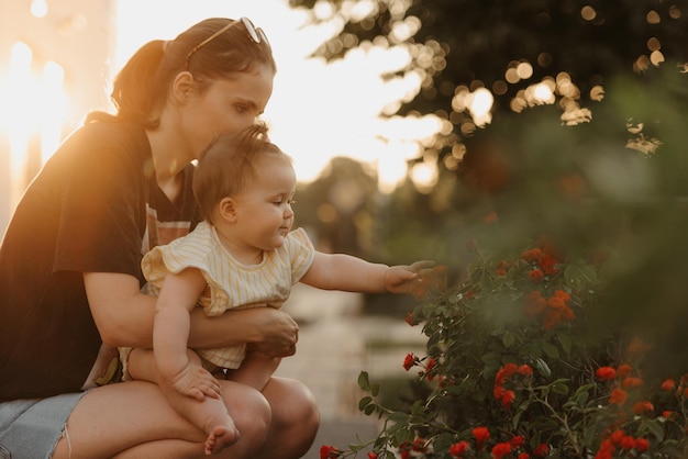 La madre tiene in ginocchio la sua bambina vicino al cespuglio di fiori nel giardino