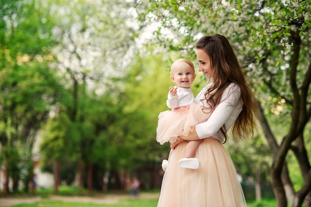 La madre tiene la sua piccola figlia tra le braccia tra alberi in fiore. Mamma e il suo bambino indossavano un abito rosa dall'aspetto familiare.