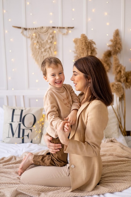 La mamma abbraccia dolcemente un piccolo bambino a casa su un letto nei toni del marrone naturale una famiglia felice con un bambino piccolo si diverte insieme