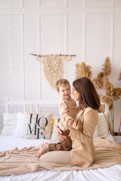 La mamma abbraccia dolcemente un piccolo bambino a casa su un letto nei toni del marrone naturale una famiglia felice con un bambino piccolo si diverte insieme