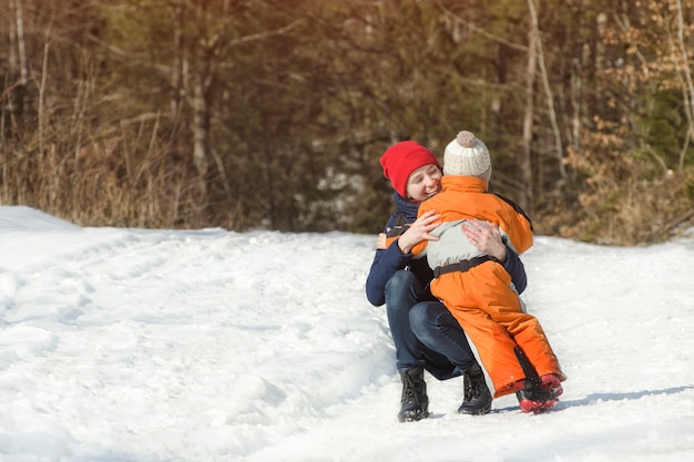 La mamma abbraccia il figlio piccolo su uno sfondo di pineta. Giorno nevoso di inverno nella foresta di conifere