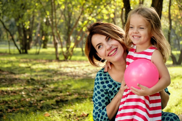 La mamma abbraccia una bambina che tiene un pallone nel parco