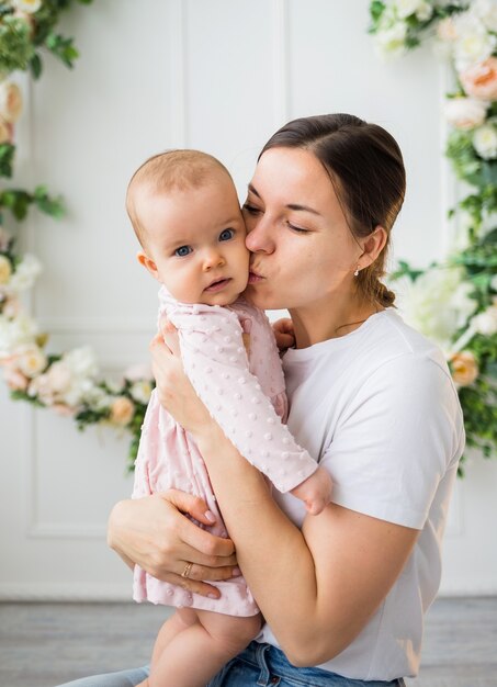 La mamma bacia la bambina su priorità bassa bianca con i fiori