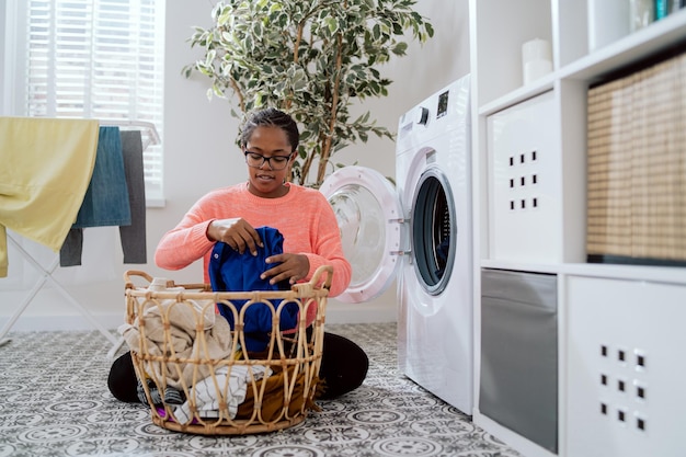 La mamma con gli occhiali fa le faccende domestiche nella lavanderia del bagno si siede sul pavimento con un cesto di vimini