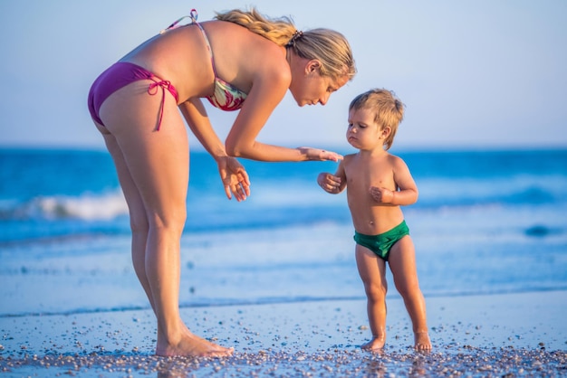 La mamma con gli occhiali gioca con un bambino seduto sulla spiaggia vicino al mare