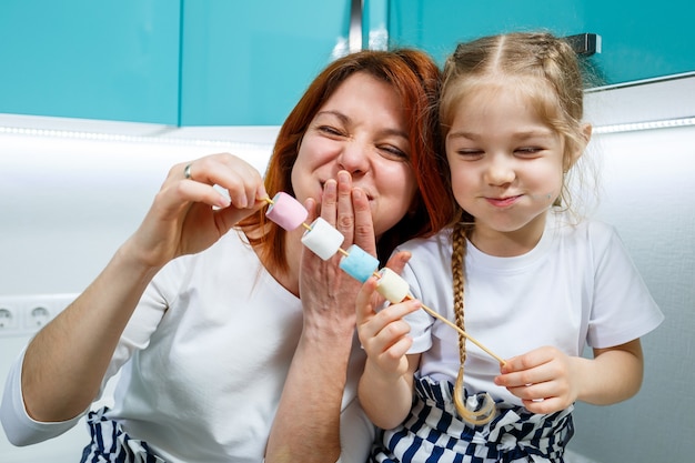 La mamma con la figlia nella cucina turchese mangia marshmallow. Belle relazioni familiari. Concetto di famiglia felice, genitori e figli felici