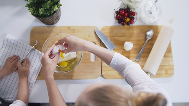 La mamma con sua figlia mette le uova crude nell'impasto per i pancake alla ricotta