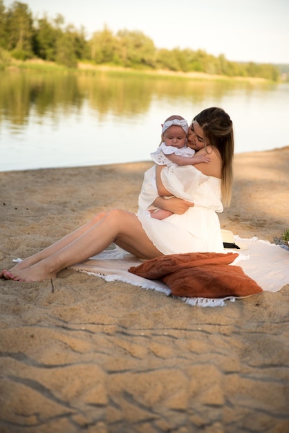 La mamma con un neonato si siede sulla spiaggia sulla sabbia la mamma tiene in braccio un neonato