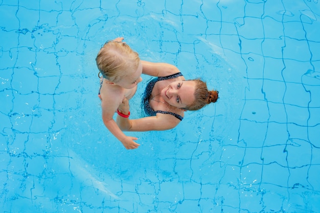 La mamma di famiglia felice insegna a sua figlia di anni a nuotare nella vista dall'alto della piscina