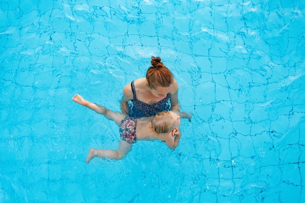 La mamma di famiglia felice insegna a sua figlia di anni a nuotare nella vista dall'alto della piscina