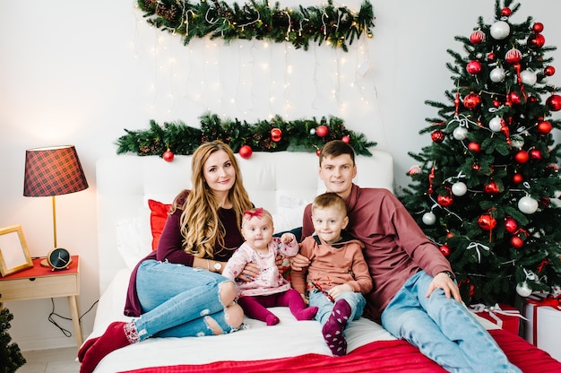 La mamma di papà abbraccia il figlio e la figlia vicino all'albero di Natale Felice Anno Nuovo e Buon Natale