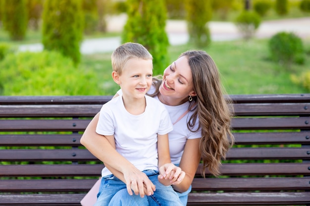 La mamma e il suo bambino nel parco su una panchina d'estate si divertono ad abbracciarsi, ridere e giocare